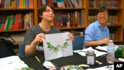 FILE - Undergraduate student Moe Lewis, left, shows her watercolor painting of peony leaves at a traditional Chinese painting class at the Confucius Institute at George Mason University in Fairfax, Va., May 2, 2018.