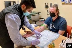 Jacob Marquez, a clinical research coordinator at Oregon Health & Science University's Knight Cancer Institute in Portland, Ore., draws blood from clinical study participant David Parker on March 14, 2022. (AP Photo/Gillian Flaccus)