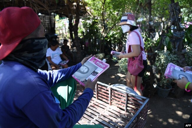 Seorang sukarelawan (kanan) untuk calon presiden oposisi dan wakil presiden saat ini, Leni Robredo, membagikan brosur kepada penduduk selama kampanye dari rumah ke rumah di kota Pasuquin, provinsi Ilocos Norte, 26 Maret 2022. (Foto: Ted ALJIBE / AFP)