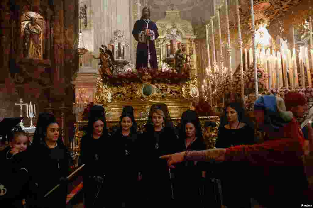 Penitentes con vestidos tradicionales de mantilla y &#39;Costaleros&#39; pertenecientes a la hermandad de Los Gitanos esperan dentro de una iglesia para participar en una procesión del Domingo de Ramos, en Ronda, España.