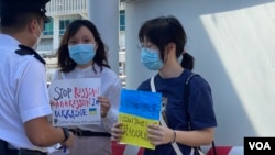 兩名香港大專女學生化名阿貓(左）及H同學，4月11日在尖沙咀天星碼頭五支旗桿下，手持聲援烏克蘭的標語進行”快閃”反戰示威，被警員截查，警告她們可能違反防疫”限聚令”。 (美國之音/湯惠芸) 
