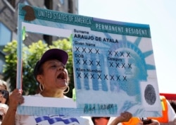 FILE - A woman holds an enlarged replica of a green card during a rally to demand immigration reform, Los Angeles, California, Oct. 5, 2013.