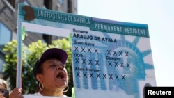 FILE - A woman holds an enlarged replica of a green card during a rally to demand immigration reform, in Los Angeles, Oct. 5, 2013.