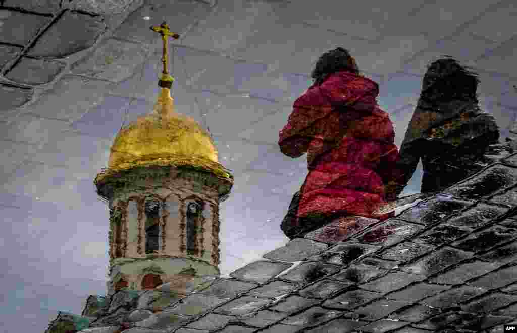 Women are reflected in a puddle as they walk across Red Square in Moscow.