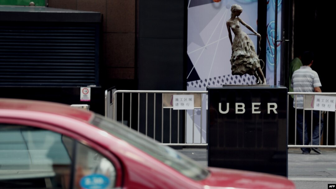 A taxi passes by an Uber station outside a shopping mall in Beijing on August 1, 2016. Ride-sharing giant Uber is to merge its China operations with local rival Didi Chuxing, reports said on August 1, ending a ferocious battle for market share in the world's second-largest economy.