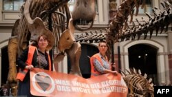 This handout picture released by climate mouvement 'Last Generation' shows two environmental activists being glued to metal bars around a display of dinosaur skeletons in the Berlin's Natural History Museum, Oct. 30, 2022. (Tenzin Heatherbell/various sources/AFP)