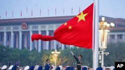 In this photo released by Xinhua News Agency, a member of the Chinese honor guard unfurls the Chinese national flag during a flag-raising ceremony marking the founding of the People's Republic of China at Tiananmen Square in Beijing on Oct. 1, 2022. 