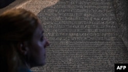 A member of the British Museum staff looks at the Rosetta Stone on Oct. 11, 2022, displayed for the exhibition "Hieroglyphs: Unlocking Ancient Egypt," which runs at the London museum Oct. 13 through Feb. 19, 2023. (Photo by CARLOS JASSO / AFP)