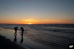 The sun sets in the horizon as Ned Ahgupuk and his girlfriend, Kelsi Rock, piggybacking their 1-year-old son, Steven, stroll along the beach on the Arctic Ocean in Shishmaref, Alaska, Friday, Sept. 30, 2022.