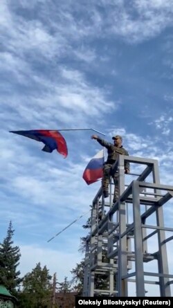 A member of the Ukrainian troop brings down a Donetsk Republic flag hoisted on a monument in Lyman, Ukraine in this screen grab obtained from social media video released on Oct. 1, 2022.