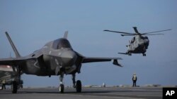 FILE - Military personnel direct F-35 jets and a helicopter on the deck of the aircraft carrier HMS Queen Elizabeth as it participates in the NATO Steadfast Defender 2021 exercise off the coast of Portugal, May 27, 2021. The alliance is holding nuclear exercises next week.