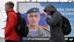 俄罗斯年轻人路过树立在圣彼得堡街头的一个在乌克兰作战受奖的俄罗斯士兵宣传画。（2022年9月5日）