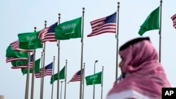 Seorang pria berdiri di bawah bendera AS dan Arab Saudi sebelum kunjungan Presiden Joe Biden, di sebuah lapangan di Jeddah, Arab Saudi, 14 Juli 2022. (Foto: AP)