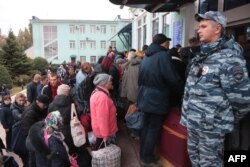 People, who arrived from Russia-annexed Kherson wait for further evacuation into Russia at the Dzhankoi's railway station in Crimea, which Moscow annexed in 2014, Oct. 21, 2022, as a Russian soldier stands by.
