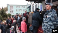 People, who arrived from Russia-annexed Kherson wait for further evacuation into Russia at the Dzhankoi's railway station in Crimea, which Moscow annexed in 2014, Oct. 21, 2022, as a Russian soldier stands by.