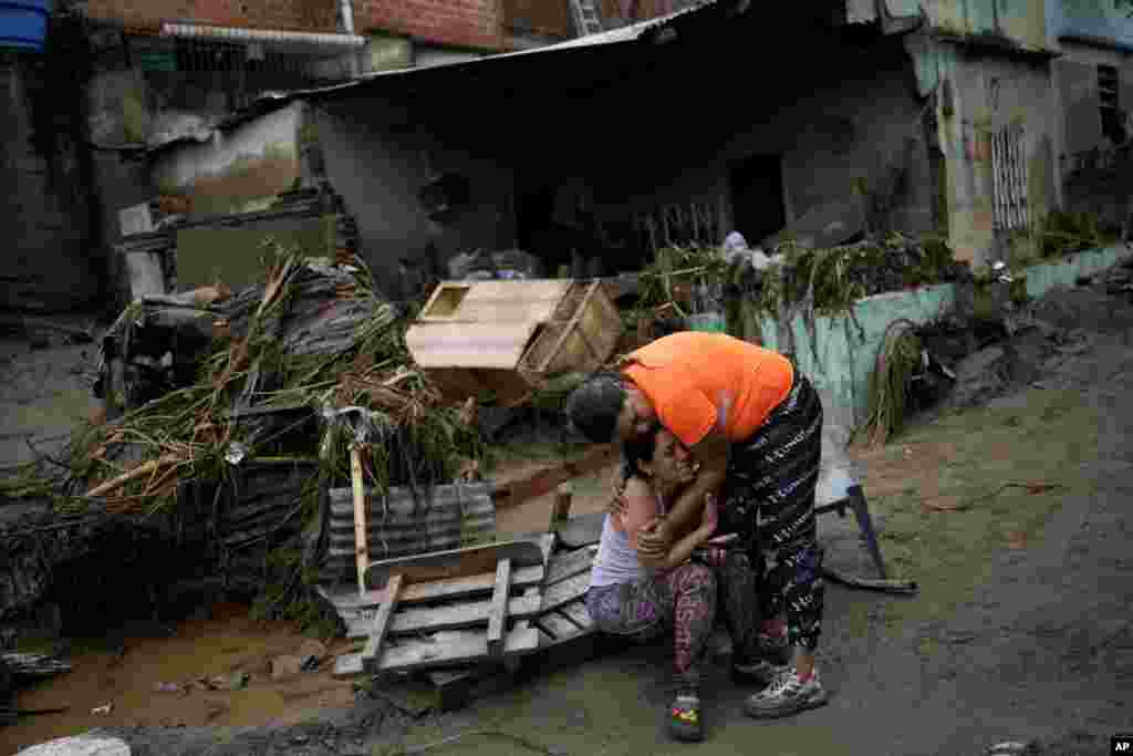 A neighbor, right, comforts a woman crying in front of her damaged home by flooding in Las Tejerias, Venezuela, after days of heavy rains caused the overflow of a river.