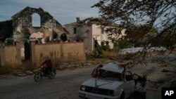 A man drives his motorcycle past a destroyed car in the retaken village of Velyka Oleksandrivka, Ukraine, Oct. 12, 2022.