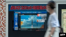 FILE - A woman walks past a public television screen in Tokyo, displaying file footage of North Korean missile launches during a broadcast about an early-morning North Korean missile launch that prompted an evacuation alert when it flew over northeastern Japan.