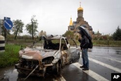 A passer-by looks at a car damaged by Russian shelling in central Bakhmut, a site of Ukraine's heavy battles against Russian troops in the Donetsk region, Ukraine, Oct. 26, 2022.