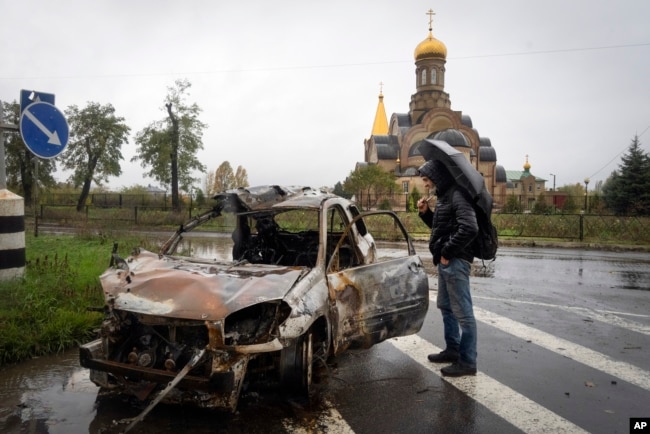 A passer-by looks at a car damaged by Russian shelling in central Bakhmut, a site of Ukraine's heavy battles against Russian troops in the Donetsk region, Ukraine, Oct. 26, 2022.