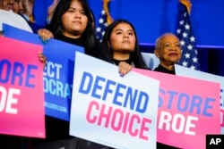 People hold signs on stage as President Joe Biden speaks about abortion access during a Democratic National Committee event at the Howard Theatre, in Washington, Oct. 18, 2022.