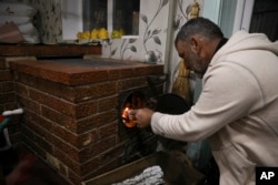 Gheorghe Batca feeds firewood into a stove that heats his home outside Chisinau, Moldova, Sunday, Oct. 16, 2022. Europe's energy crisis, triggered by Russia slashing natural gas flows amid its war against Ukraine, has forced some people to turn to cheaper firewood. (AP Photo/Aurel Obreja)