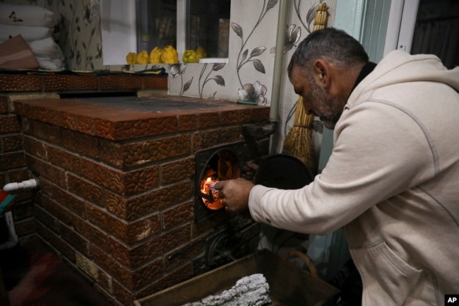 Gheorghe Batca feeds firewood into a stove that heats his home outside Chisinau, Moldova, Sunday, Oct. 16, 2022. Europe's energy crisis, triggered by Russia slashing natural gas flows amid its war against Ukraine, has forced some people to turn to cheaper firewood. (AP Photo/Aurel Obreja)