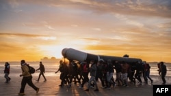 Migrants carry a smuggling boat on their shoulders as they prepare to embark on the beach of Gravelines, near Dunkirk, northern France, Oct. 12, 2022, in a attempt to cross the English Channel.