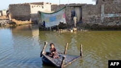 Seorang anak perempuan menggunakan ranjang bayi untuk melewati jalanan yang terendam banjir di Sohbatpur, distrik Jaffarabad, provinsi Balochistan, Pakistan, pada 4 Oktober 2022. (Foto: AFP/Fida Hussain)