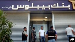 Lebanese security officers stand at the entrance of a Byblos Bank branch that was broken into by depositor Ali Hodroj holding a handgun, firing a warning shot, and demanding about $40,000 of his trapped savings, in Tyre, south Lebanon, Oct. 4, 2022. 