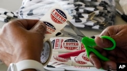 Petugas Tempat Pemungutan Suara (TPS) tampak memotong stiker "I Voted in Hinds County" untuk dibagikan kepada para pemilih di salah satu TPS di Bolton, Mississippi, pada 7 Juni 2022. (Foto: AP/Rogelio V. Solis)