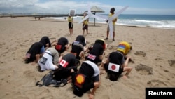 FILE - Environmental activists with flags on their backs bury their heads in the sand on Durban's beachfront, December 2, 2011. The protest aimed to highlight nations failing to act effectively to prevent climate change. (REUTERS/Mike Hutchings)