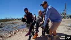 FILE - Rescuers help evacuate a woman in a wheelchair as they carry her to a waiting boat in the aftermath of Hurricane Ian, on Florida's Pine Island, Oct. 2, 2022.