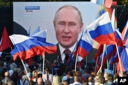 FILE - People watch on a large screen, as Russian President Vladimir Putin delivers his speech after a ceremony to sign the treaties for four regions of Ukraine to join Russia in Moscow's Kremlin, during a meeting in Sevastopol, Crimea, Friday, Sept. 30, 2022.