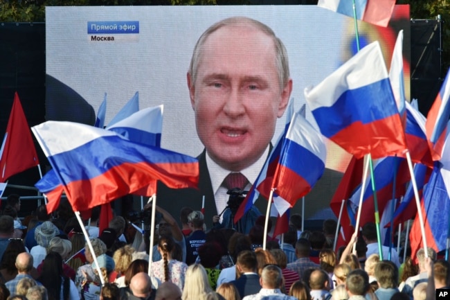 FILE - People watch on a large screen, as Russian President Vladimir Putin delivers his speech after a ceremony to sign the treaties for four regions of Ukraine to join Russia in Moscow's Kremlin, during a meeting in Sevastopol, Crimea, Friday, Sept. 30, 2022.