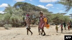 FILE - Women and children from the pastoral Turkana community in northwest Kenya carry cans as they search for water among shallow wells dug on a riverbed on Sept. 27, 2022. 