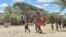 FILE - Women and children from the pastoral Turkana community in northwest Kenya carry cans as they search for water among shallow wells dug on a riverbed on Sept. 27, 2022. 