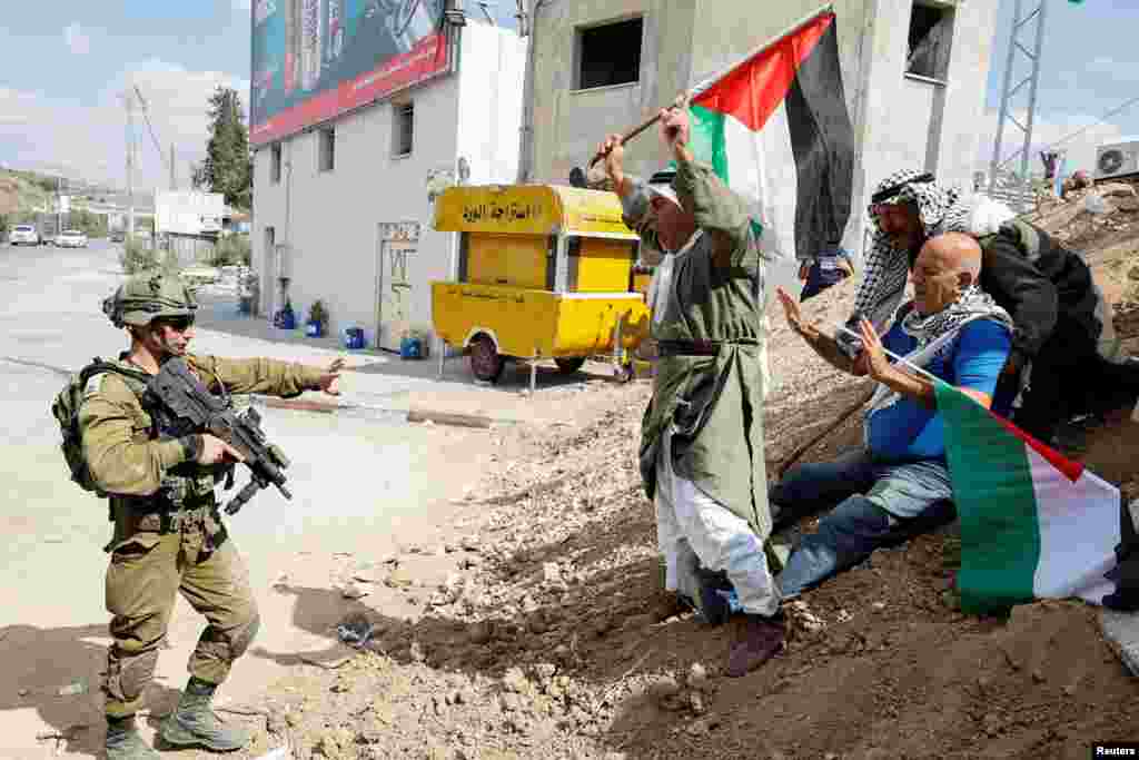 Demonstrators hold Palestinian flags in front of an Israeli soldier during a protest demanding Israel reopen closed roads leading to Nablus, in Deir Sharaf, in the Israeli-occupied West Bank.