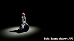 A performer looks up while sitting on the stage of the Trafo House of Contemporary Arts in Budapest, Hungary, Sept. 19, 2022. (AP Photo/Bela Szandelszky)