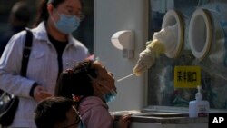 A man wearing a face mask helps a child to get her routine COVID-19 throat swab at a coronavirus testing site in Beijing, Oct. 6, 2022.