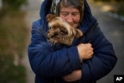 A woman warms her dog in Kivsharivka, Ukraine, Sunday, Oct. 16, 2022. (AP Photo/Francisco Seco)