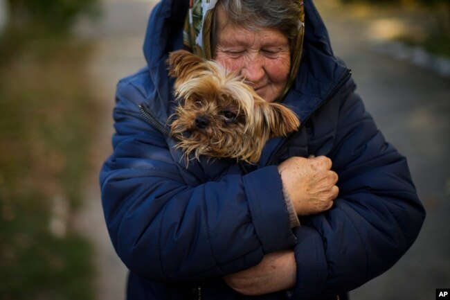 A woman warms her dog in Kivsharivka, Ukraine, Sunday, Oct. 16, 2022. (AP Photo/Francisco Seco)