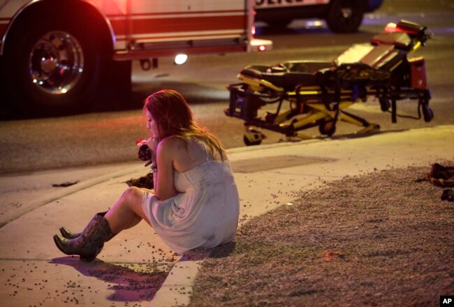 FILE - A concert attendee sits on a curb at the scene of a deadly mass shooting at a music festival on October 1, 2017 in Las Vegas, Nevada. (AP Photo/John Locher, File)