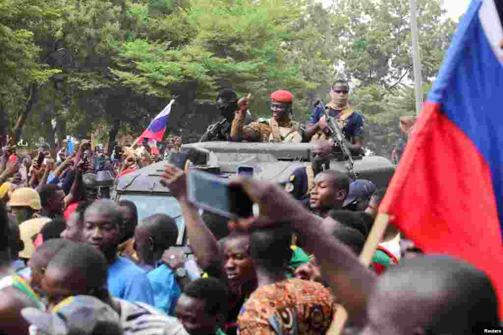 O novo líder auto-declarado do Burkina Faso, Ibrahim Traore, é recebido por apoiantes que seguram as bandeiras russas ao chegar à televisão nacional num veículo blindado em Ouagadougou, a 2 de Outubro de 2022.