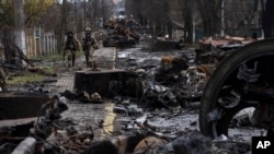 Sejumlah tentara Ukraina berjalan di tengah puing-puing tank milik pasukan Rusia yang hancur di Bucha, wilayah pinggiran Kyiv, pada pada 3 April 2022. (Foto: AP/Rodrigo Abd)