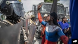 Seorang demonstran yang melumuri badannya dengan cat bermotif bendera Rusia berdebat dengan polisi dalam aksi protes di depan kedutaan besar AS di Port-au-Prince, Haiti, pada 17 Oktober 2022. (Foto: AP/Odelyn Joseph)