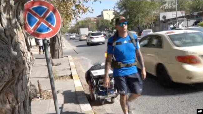 In this frame grab from video, 41-year-old Santiago Sanchez, a Spanish man who was documenting his travel by foot from Madrid to Doha for the 2022 FIFA World Cup, carries a suitcase in a wheeled cart, in Sulaymaniyah, Iraq, Sept. 28, 2022.
