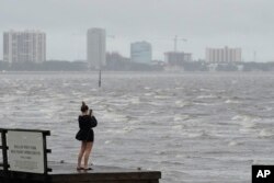 A woman takes photos of the surf on Tampa Bay ahead of Hurricane Ian, Sept. 28, 2022, in Tampa, Fla.