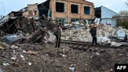 People stand by a crater left near a railway yard of the freight railway station in Kharkiv, which was partially destroyed by a missile strike, Sept. 28, 2022.