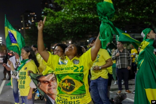 Supporters of Brazilian President Jair Bolsonaro, who is running for another term, celebrate partial results after general election polls closed outside his family home in Rio de Janeiro, Brazil, Sunday, Oct. 2, 2022. (AP Photo/Bruna Prado)